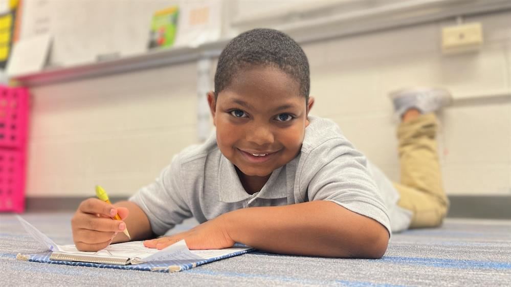 boy laying on ground working on a clipboard